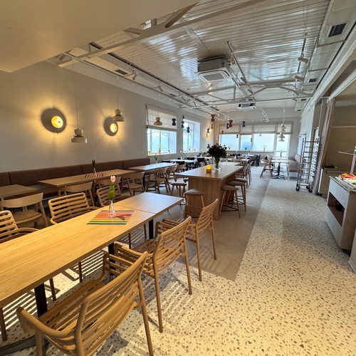 Cozy breakfast dining room with wooden tables, a central bar-style table, pendant lamps and a fruit buffet.