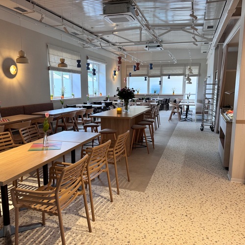 Spacious, bright hotel dining room with wooden tables, a bar island, hanging lamps and single tulips