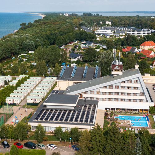 Seaside hotel with a triangular wing, a pool with loungers, solar panels, a beach and camping cabins.