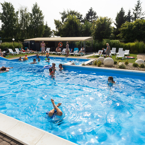 Hotel outdoor pool with loungers, a shaded shelter and families swimming with inflatable toys.