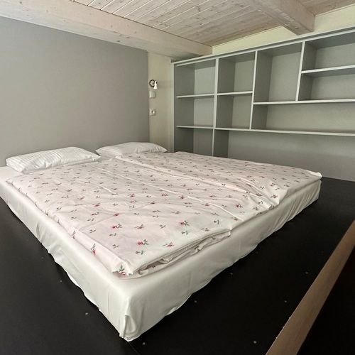 Cozy bedroom with a low double bed in floral bedding, built-in shelves, a wooden ceiling and bedside lamps.