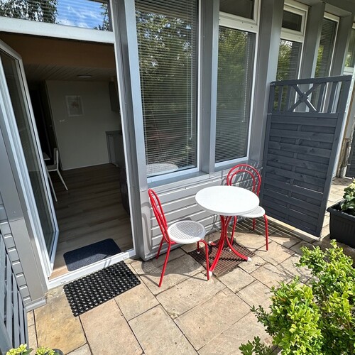 Private room terrace with a white round table, two red chairs, glass doors, a windbreak and flower pots