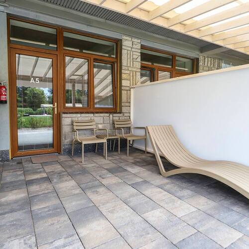 Private terrace of room A5 with a sunbed and two chairs, covered by a pergola, stone facade and glass doors.