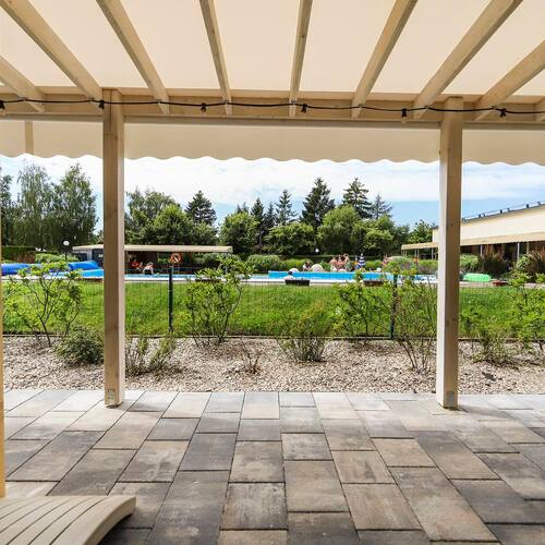 Covered terrace with clinker flooring, view of the outdoor pool, loungers, a lawn and the poolside building.