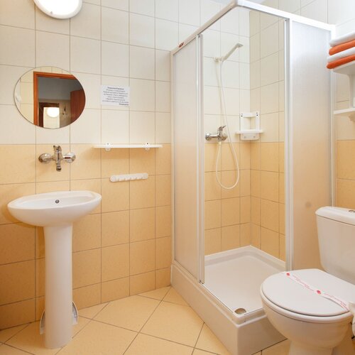 Hotel bathroom with a shower enclosure, a pedestal sink, a toilet with a sanitary seal and towels on a shelf.