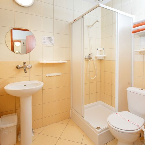 Bright, clean hotel bathroom with a shower enclosure, a freestanding sink, a toilet with a seal and a shelf of towels