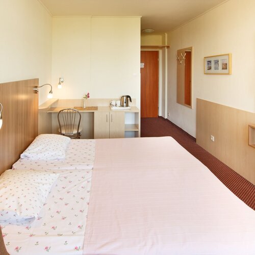 Cozy double room with a large bed, wooden headboard, bedside lamps, a desk with a kettle and a TV