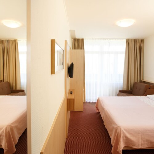 Room with a double bed, wooden headboards, a sofa, TV, a large window with sheer curtains and warm lighting