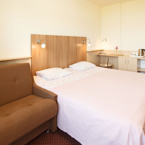 Double room with a large bed, a brown sofa, a headboard with lamps and a desk with a kettle and cups.