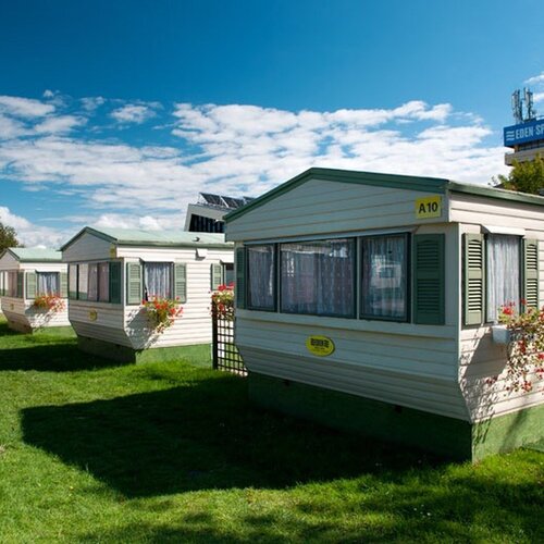 A row of mobile homes with green shutters, flowers in boxes and a well-kept lawn, with the Eden Spa building in the background