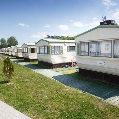 A row of mobile holiday homes along wooden paths, green lawn, shuttered windows and children's bikes at the entrances