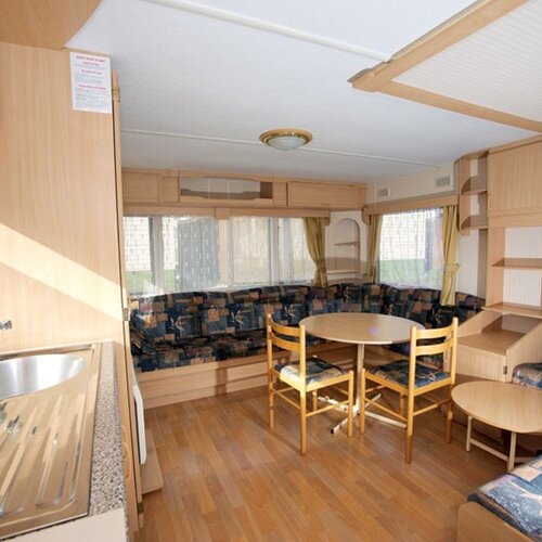 Atmospheric living room of a mobile home with light wooden interior, a kitchen sink, a table and a corner sofa