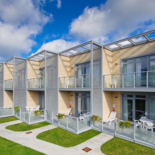 Modern rooms with wooden facade, private balconies and terraces, glass balustrades, sunbeds and flowers.