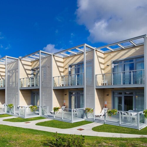 Modern two-storey hotel building with private glass terraces and balconies, sunbeds and flower pots.