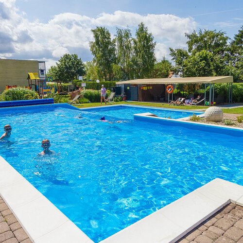Hotel outdoor pool with crystal-blue water, loungers, a covered patio, a playground and children swimming.