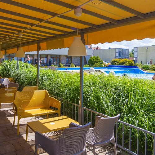Covered terrace with yellow awnings and seating, view of the pool, greenery and a child playing.