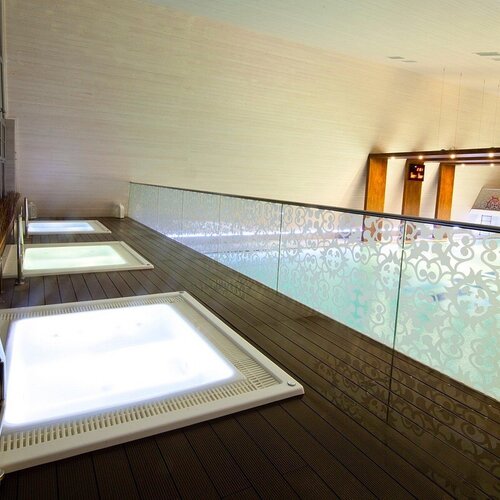 Spa area with three illuminated built-in jacuzzis on a wooden terrace and a decorative glass balustrade