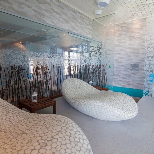 Modern spa area with two stone-patterned loungers, glass partitions with decor, a reed screen and a turquoise accent.