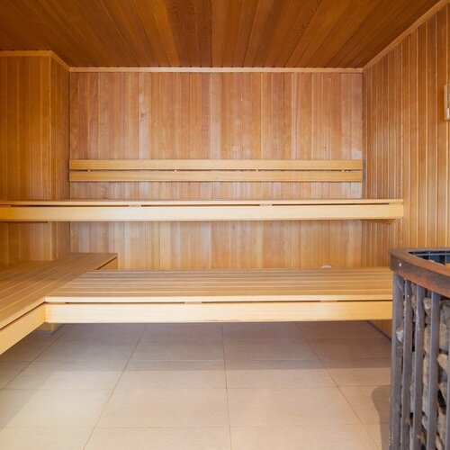 Hotel sauna of light wood, multi-level benches, a stone heater and a light tiled floor