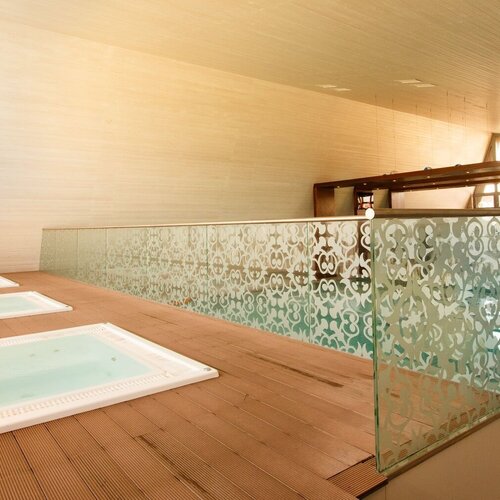 Spa: three built-in jacuzzis on a wooden terrace, a decorative sandblasted glass balustrade and an indoor pool by large windows.