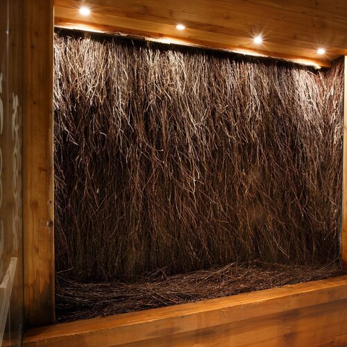Indoor spa feature wall of densely arranged twigs framed in warm wood, softly lit from above with frosted glass panels.