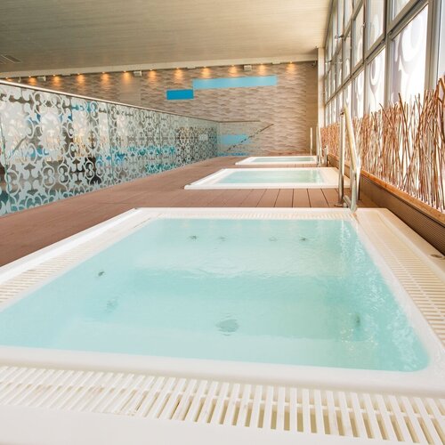 Three glass-enclosed jacuzzis in the hotel spa, a wooden jetty, decorative glass panels and natural sticks by the window, relaxing atmosphere.
