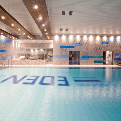 Hotel's indoor pool with a water surface, handrails, relaxing seats, wooden beams and ambiance.