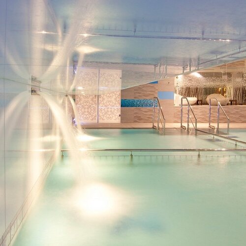 Interior of the hotel's spa: illuminated pool with water cascades, steps and loungers in an elegant, modern interior.