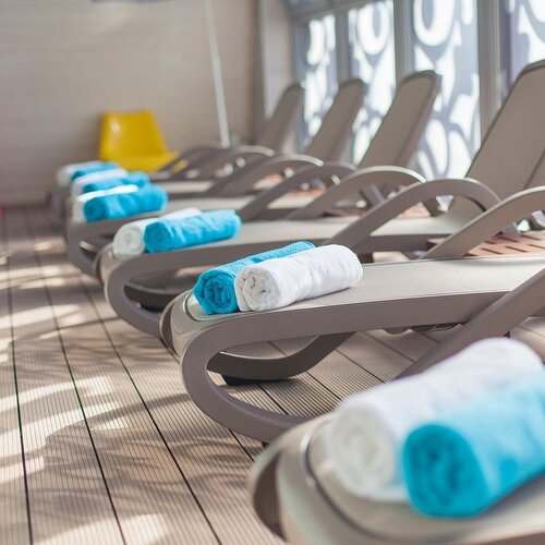 A row of loungers on the spa terrace, each with a white and turquoise towel; lattice window screens cast decorative patterns.