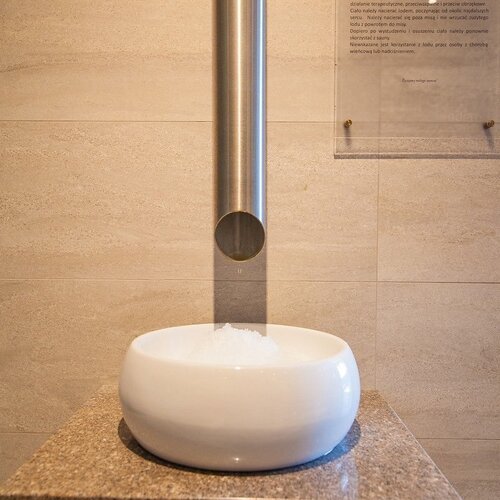 A white bowl of crushed ice under a steel spout in the spa — an ice bowl for cooling down after the sauna.