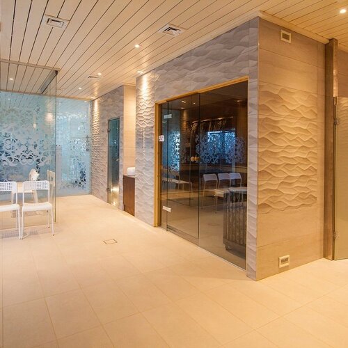 Elegant, cozy spa area with textured walls, glass cabins, white chairs and a restroom.
