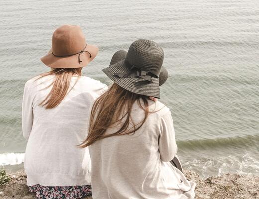 Two women in hats sitting on a cliff, silently admiring the calm sea and waves