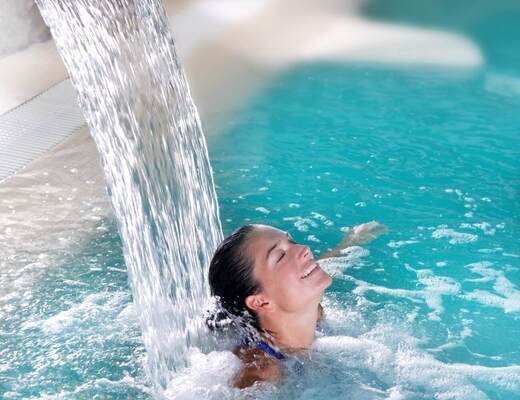 A woman relaxing under a massage water jet in a blue hotel spa pool, bubbles and a waterfall