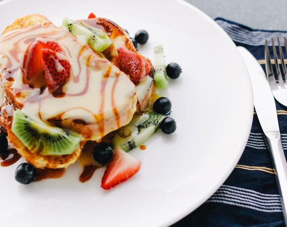 French toasts with creamy sauce, caramel and fresh fruits (strawberries, kiwi, blueberries) on a white plate