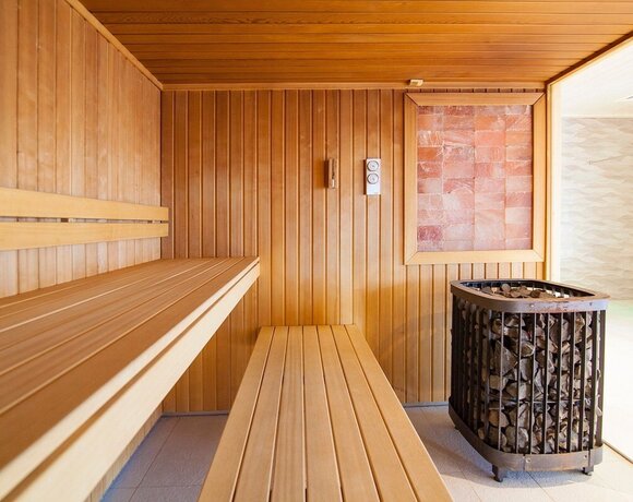 Drewniana sauna hotelowa z dwoma poziomami ławek, piecem z kamieniami i ścianą solną, relaksująca atmosfera spa