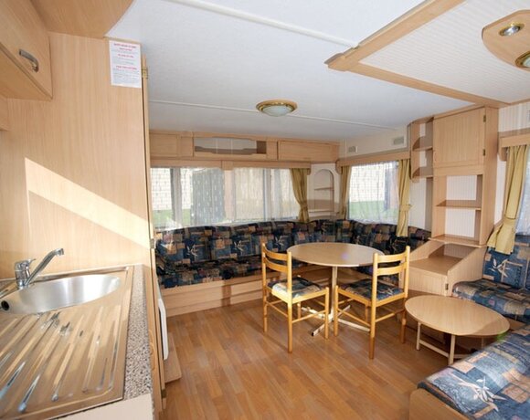 Klimatyczny salon domku mobilnego z jasnym drewnianym wnętrzem, kuchennym zlewem, stołem i narożną kanapą