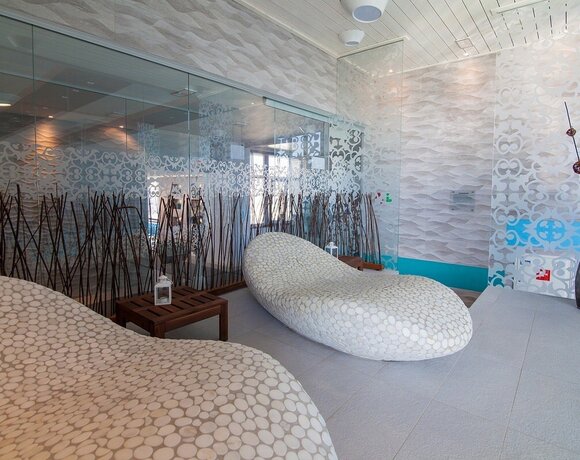 Nowoczesna strefa spa z dwiema leżankami w kamiennym wzorze, szklanymi przegrodami z dekorem, trzcinowym parawanem i turkusowym akcentem.