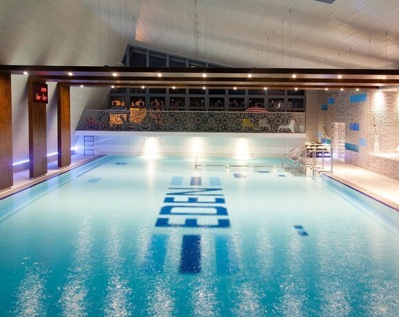 Elegant, illuminated indoor hotel pool with wooden ceiling beams, a decorative mezzanine and stairs into the water