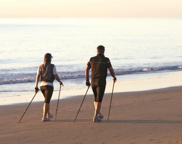 A couple walking with Nordic walking poles along the seashore at sunrise, a calm beach and gentle waves