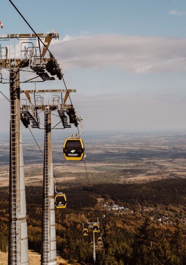 Yellow gondola cable cars above forested slopes leading to a mountain resort, with panoramic valley and village views