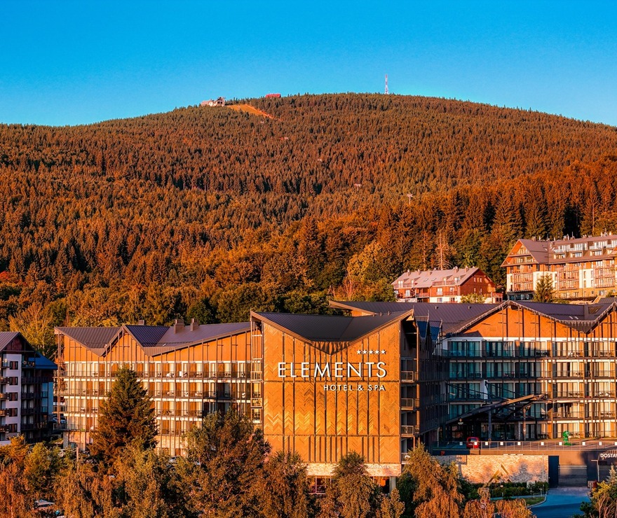 Elements Hotel & Spa with wooden façade and balconies at sunset, framed by dense forest and rolling mountain views