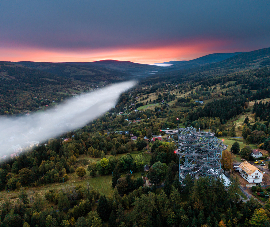 Sunset mountain valley with mist, forest trails and a spiraling treetop observation tower above countryside lodges.