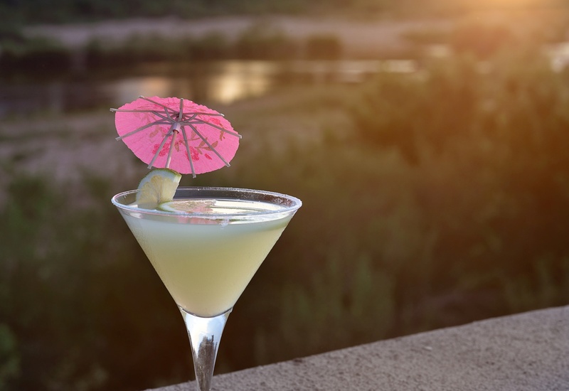 Refreshing citrus cocktail in a martini glass with lime wedge and pink paper umbrella at sunset