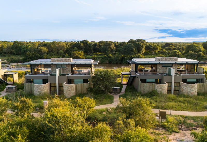 Modern riverfront safari suites with stone facades, private terraces and rooftop lounges overlooking a tree-lined riverbank
