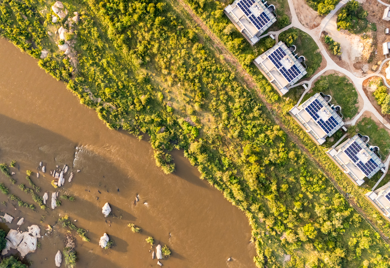 Riverside villas with solar-panel roofs, winding paths and private terraces along a green riverbank.