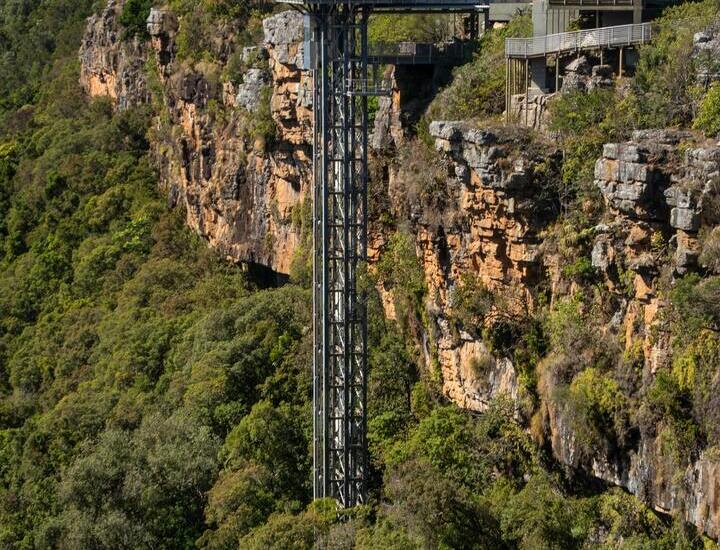 Cliffside lodge with covered observation decks and vertical glass elevator descending into lush gorge, panoramic valley views