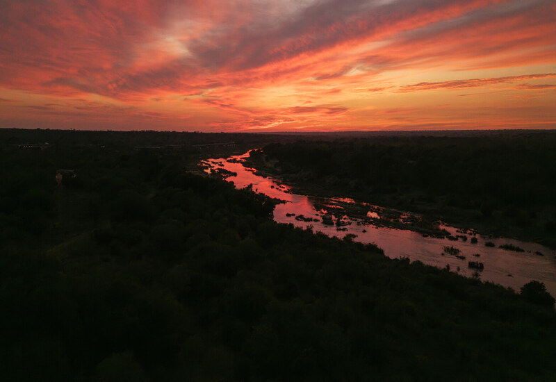 Fiery sunset sky over a winding river reflecting red light, with silhouetted riverbanks and dense wilderness