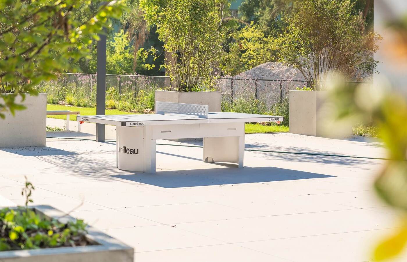 Stół do ping-ponga na słonecznym tarasie hotelowym, otoczony donicami i zielenią, strefa rekreacji.