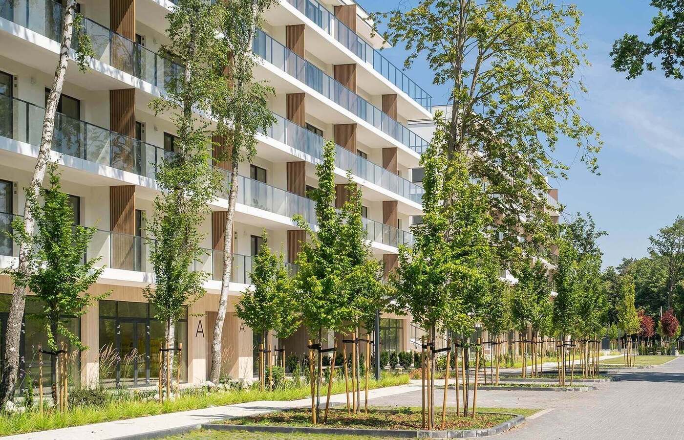 Nowoczesny hotel z przeszklonymi balkonami, alejką obsadzoną drzewami i zielonym parkowym otoczeniem