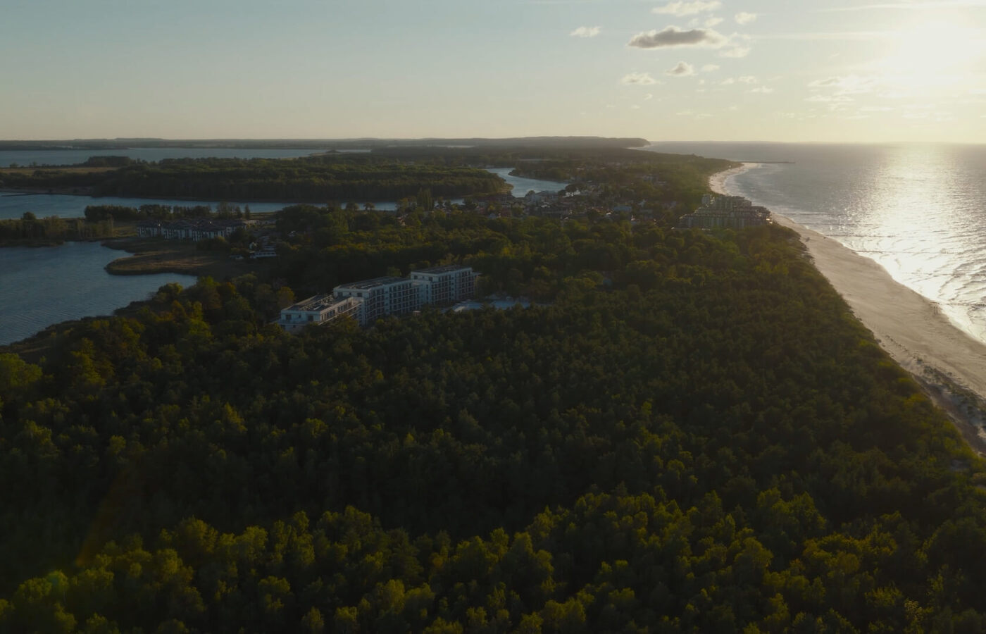 Ośrodek w sosnowym lesie przy długiej piaszczystej plaży o zachodzie słońca, z widokiem na morze i zatokę.